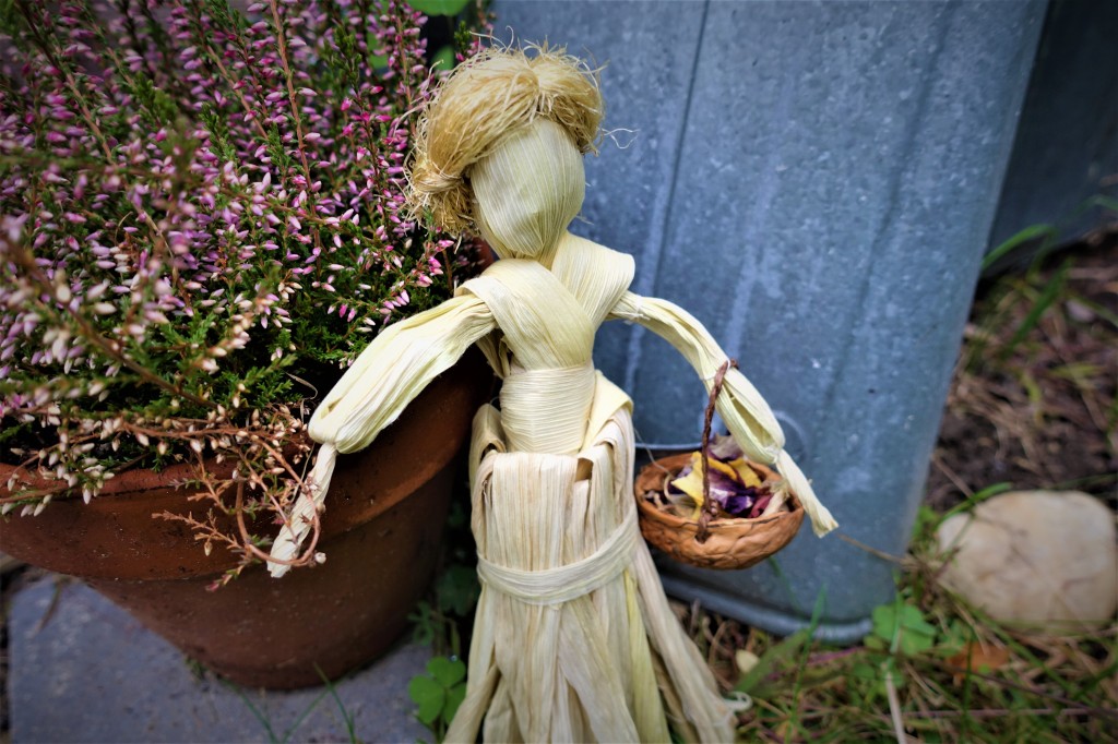 A doll made out of corn husks with blond hair and a basket in her hand