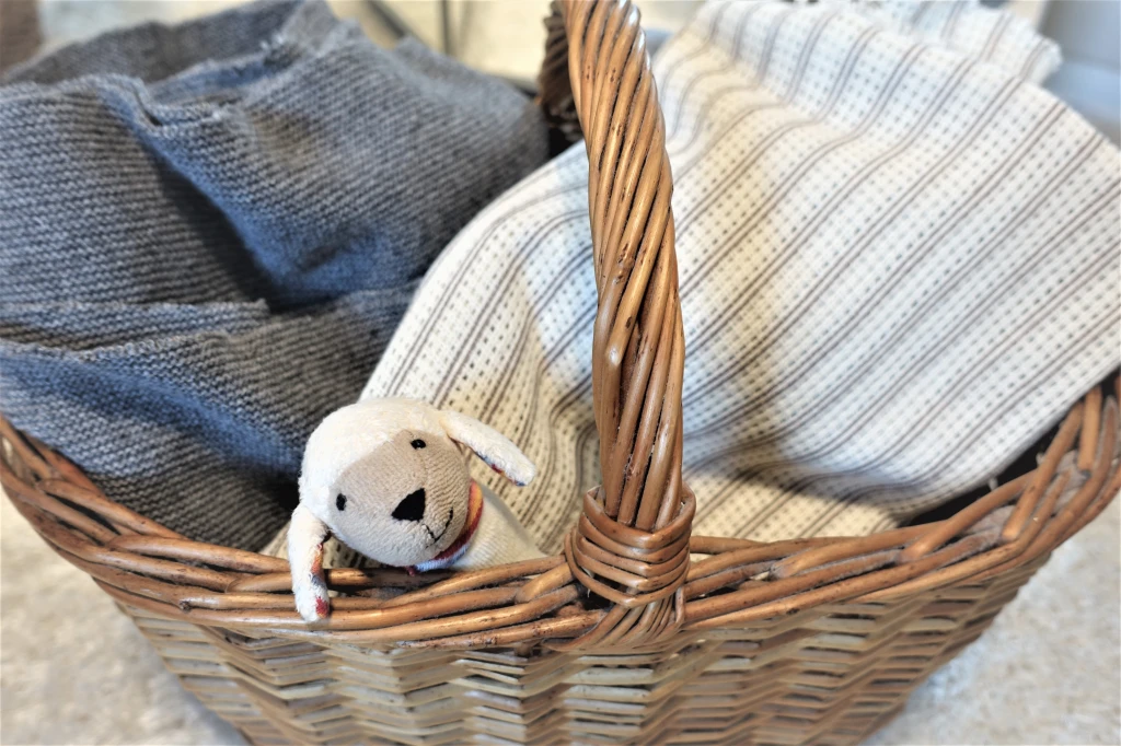 A plush animal sheep lying in a wooden basket full with materials 